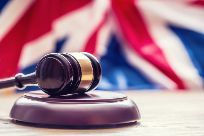 Judges wooden gavel with UK flag in the background.