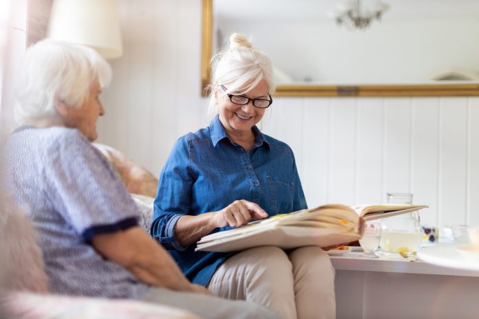 Senior woman and her adult daughter looking at photo album together on couch in living room