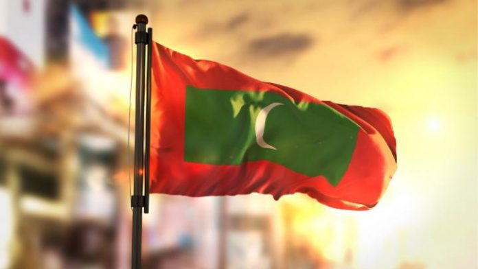 maldives-flag-against-city-blurred-background-at-sunrise-backlight-picture-id686175994