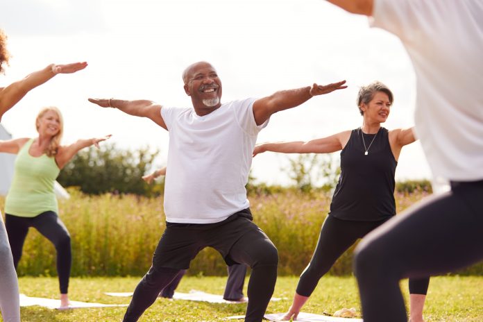 Female Teacher Leading Group Of Mature Men And Women In Class At Outdoor Yoga Retreat