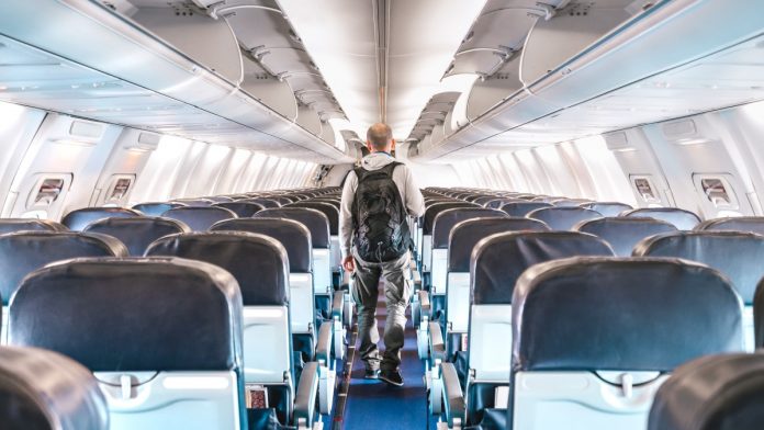 A lonely passenger walking down an empty airplane aisle.