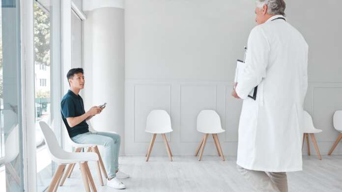 Shot of a young man using a cellphone while sitting in the waiting room of a clinic