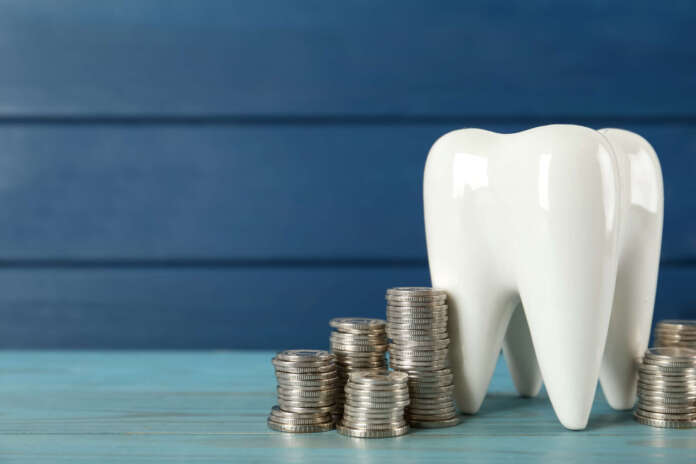 Ceramic model of tooth and coins on light blue wooden table, space for text. Expensive treatment