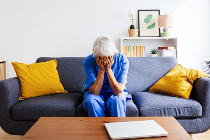 Senior nurse feeling overwhelmed sitting on sofa after hard work day in hospital