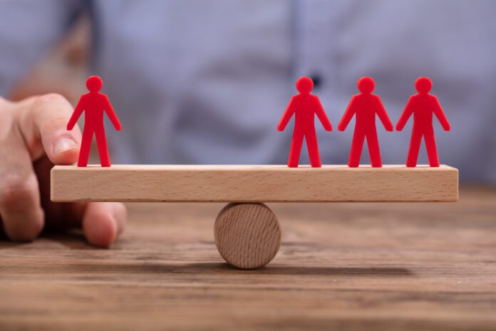 AdobeStock: 252388232 Businessperson Showing Imbalance Between Red Figures On Seesaw
