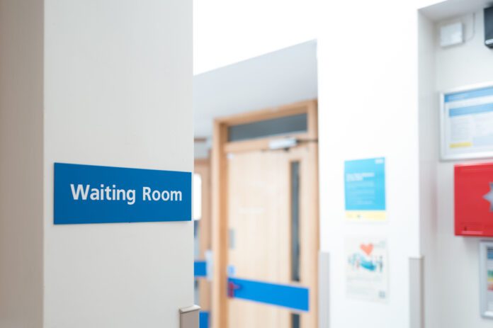 Typical British hospital and GP waiting room sign seen within a patient's medical waiting area. Corridors lead to doctors offices and medical assessment rooms.