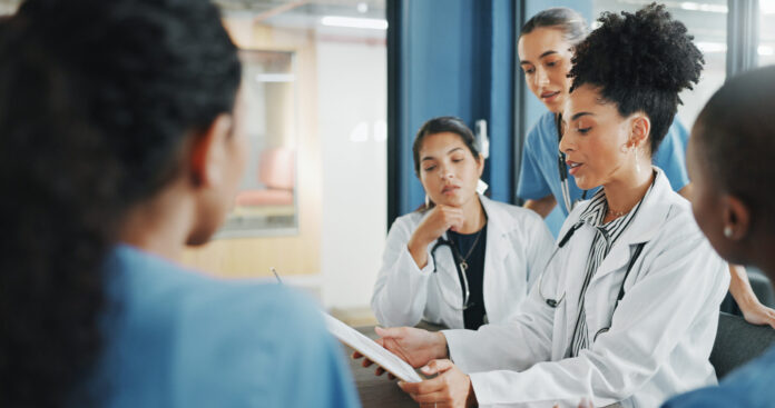 Doctors, nurse and women on clipboard in meeting, collaboration or teamwork for hospital planning, medical or life insurance. Talking, leadership and healthcare workers on paper in diversity research