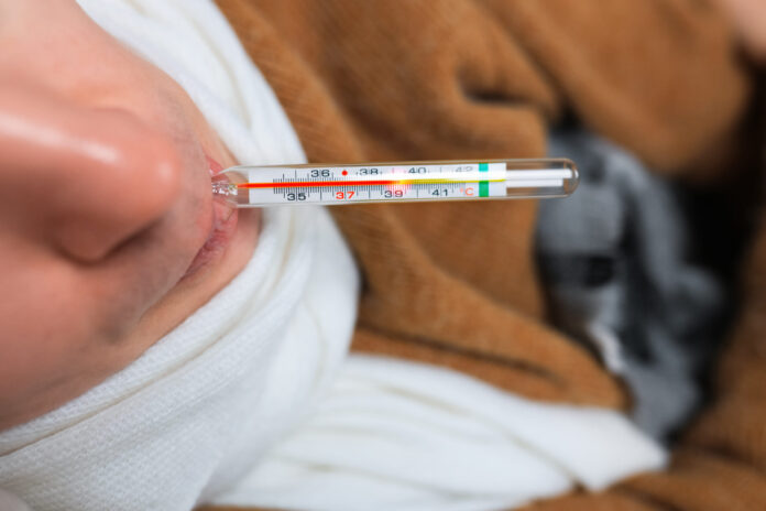 Close up of sick man with scarf holding glass thermometer in mouth showing high fever temperature.